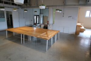 Ruimte in het Gedempt Hamerkanaal met een grote houten tafel, hangende planten en een minimalistisch interieur.